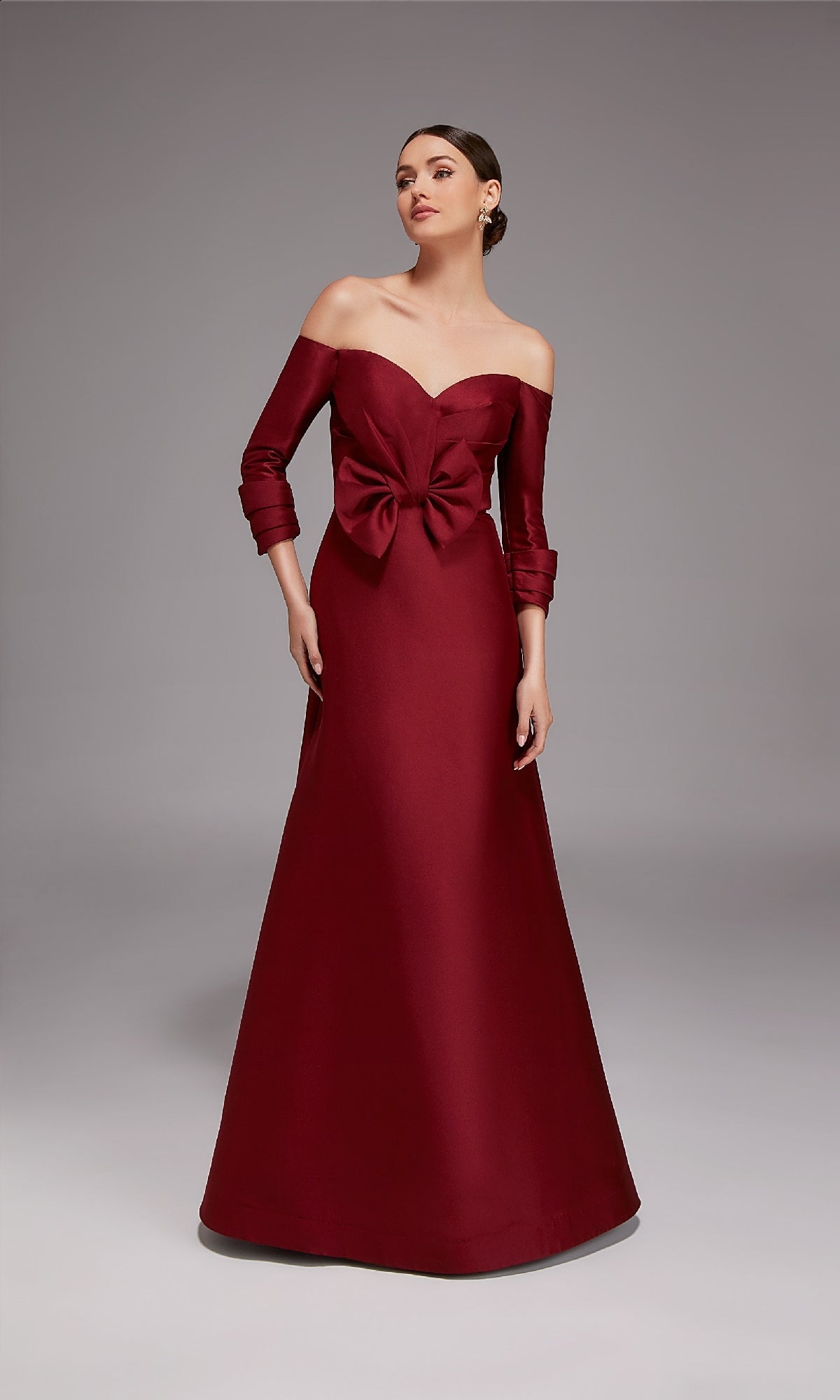 A woman wearing the Alyce 27859 long formal dress in burgundy with three-quarter sleeves and a large waist bow stands against a plain gray background.